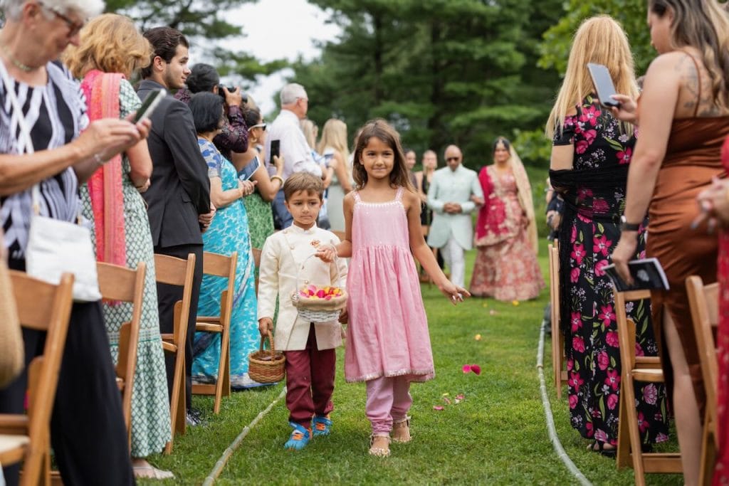 Two children throw flowers down the aisle while an out of focus bride walks in the distance with her uncle