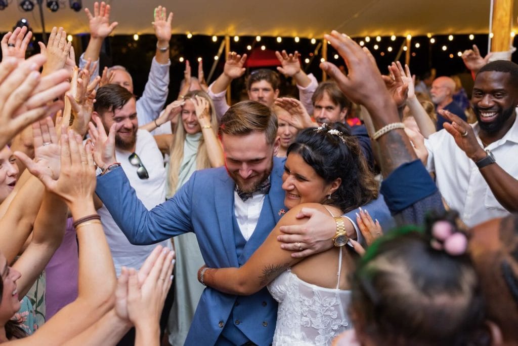 A newlywed couple surrounded by friends on the dance floor at their reception
