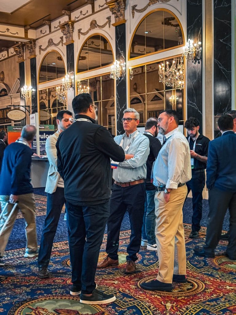 Three men are speaking in a hallway at an expo