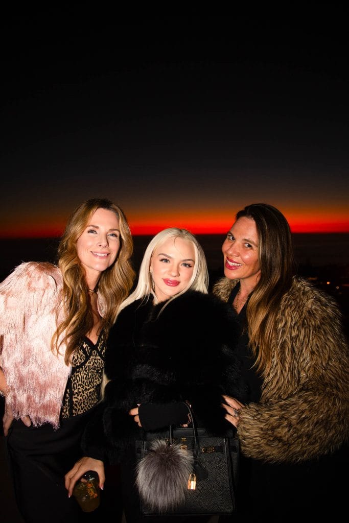 Three women pose for a photo at a party as the sun sets behind them