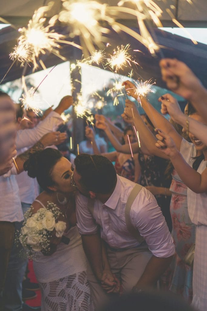 Couple kissing with people celebrating holding sparklers